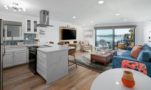 Bay Views- Living room with smart TV, comfortable couch and 2 lounge chairs. Kitchen with bar seating, 2-person dining table, and electric stove/range.