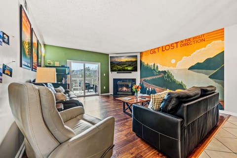 Spacious open living room with seasonal gas fireplace, 65" smart tv, leather reclining sofas and iconic mural wall