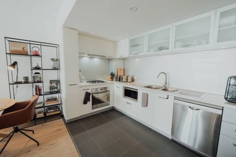 Prepare culinary delights in this modern kitchen, featuring sleek white cabinetry, stainless steel appliances, and a stylish open shelving unit.