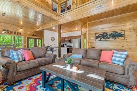 Rustic living room with leather sofas and a colorful area rug in a wood-paneled cabin.