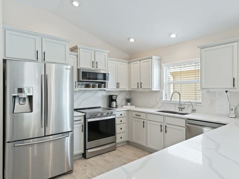 Well-lit kitchen with all stainless steel appliances.