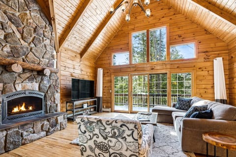 Open-concept living room with vaulted pine
    ceiling, stone fireplace, and french doors
    to the deck