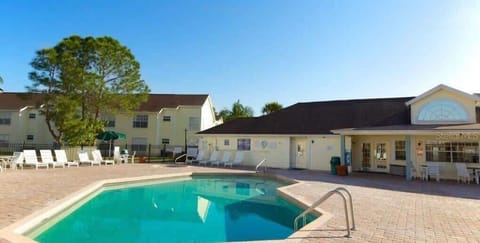 Outdoor pool area with lounge chairs and a clubhouse under clear skies