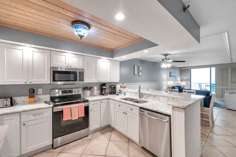 Bright kitchen w/ white cabinetry, stone counters, & warm wood ceiling accents for a clean coastal feel.
