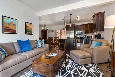 This spacious living room offers a comfy sectional, accent pillows, and beautiful wall art, all within a modern open-concept layout. It seamlessly connects to the kitchen and dining area for a welcoming and social environment.