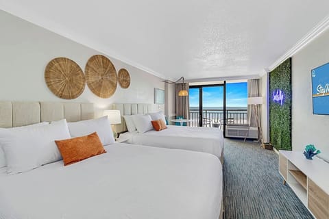 Bright, stylish oceanfront suite with two queen beds, a scenic balcony view, and modern decor. Features a lush accent wall with neon lighting, cozy seating area, and a large Smart TV. Perfect for a relaxing beach getaway!