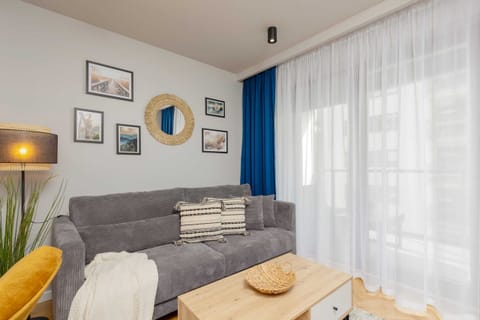 A cozy living area with a grey sofa, colorful cushions, and large windows letting in natural light.
