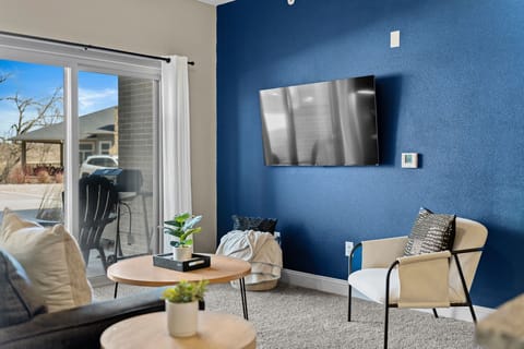 Bright living space anchored by a bold accent wall, wall-mounted TV, and comfortable seating. Natural light pours in through the sliding doors, creating an easy spot to unwind, stream your favorites, or step outside to the patio.