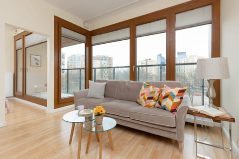 A bright living room featuring a comfortable sofa with colorful cushions, a coffee table, and large windows offering plenty of natural light.