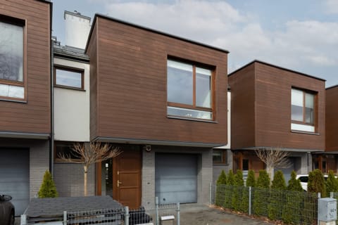 An exterior view of modern townhouses with wooden paneling and well-maintained landscaping.
