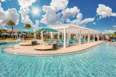 Resort-style pool area w/ curved loungers & palm accents, perfect for sunny afternoons.
