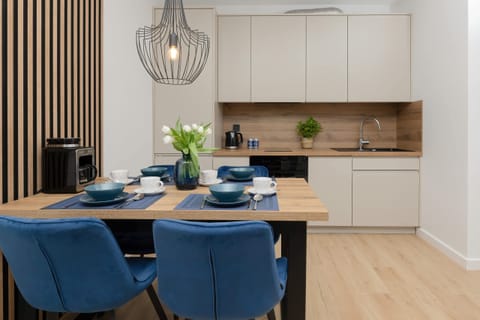 A dining area with blue chairs and a wooden table, adjacent to a modern kitchen with sleek cabinetry.
