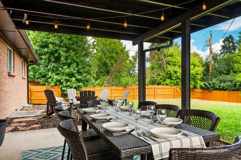 Covered patio with a large dining table, string lights, and comfy seating. Steps from the fire pit and fully fenced yard—perfect for meals, coffee, and relaxing outdoors.