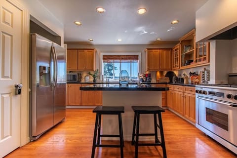 The kitchen features a very large island, gas range stovetop, two sinks, and a large stainless steal refrigerator.
