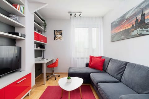 A cozy living room with a gray sofa, red accents, and a modern TV unit.
