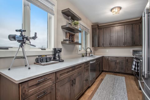 The kitchen with dark wooden cabinets, floating shelves, and a dishwasher. Functionality meets style in this cozy and rustic space.