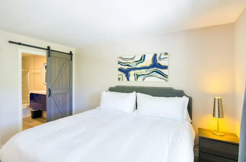 Bedroom with king bed, gray headboard, barn‑style sliding door, and coastal art
