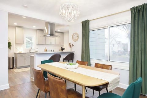 - Dining area with modern crystal light fixture   - Large window with green curtains and natural light   - Open bar seating connects space to the kitchen