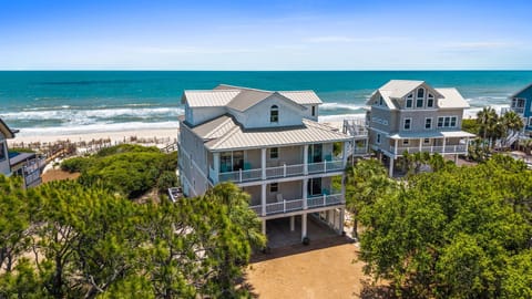 Aerial view of beachfront vacation rental surrounded by coastal greenery, with direct access to the sandy shore and turquoise waters beyond.
