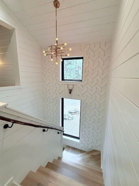 Ascend the stairs and be captivated by the seamless fusion of the stair accent wall, complementing the mid-century chandelier above with the breathtaking view of the forest outside.