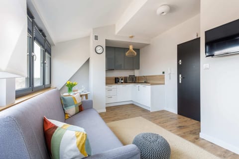 Another living room with a gray corner sofa, bright cushions, and a floor lamp, with large windows offering plenty of natural light.