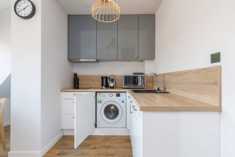 A compact kitchen with white cabinets, wooden countertops, and a built-in washing machine for added convenience.