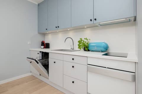 A minimalist kitchenette with white cabinetry, open shelving, and a pop of color from kitchen accessories.