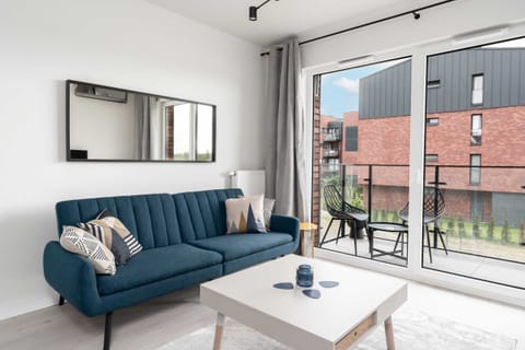 A modern living room featuring a stylish blue sofa, a coffee table, and access to a balcony with a scenic view.
