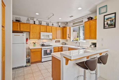 This functional U-shaped kitchen combines classic oak cabinetry with bright white countertops and tiled surfaces. It is fully equipped with modern white appliances, including a Frigidaire refrigerator and a gas range with an overhead microwave.