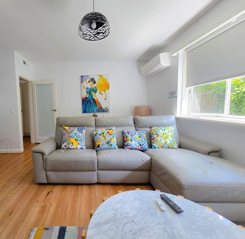 Bright modern lounge, grey sofa, AC, garden light—relax in style
