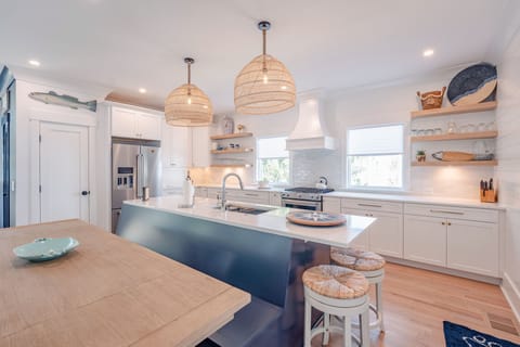 Two round counter stools with woven seats are slipped under the right end of the kitchen island for extra seating. White kitchen cabinets fill the kitchen space with stainless steel appliances and a navy kitchen island.