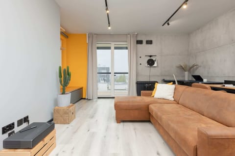 A modern, industrial-style living room with concrete walls, a comfortable orange sofa, and sleek lighting.