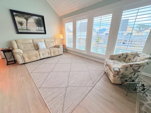 Unwind in your bright living space with plush seating and coastal artwork, where large windows invite natural light to warm your stay.