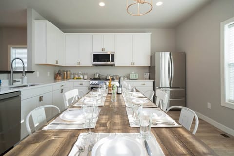Gather and enjoy meals in this bright, modern kitchen featuring sleek white cabinetry, stainless steel appliances, and a spacious farmhouse-style dining table set for your entire group. With plenty of counter space and all the essentials.
