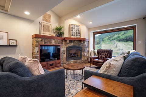 Cozy up by your stone fireplace with mountain views through expansive windows, perfect for relaxing evenings.