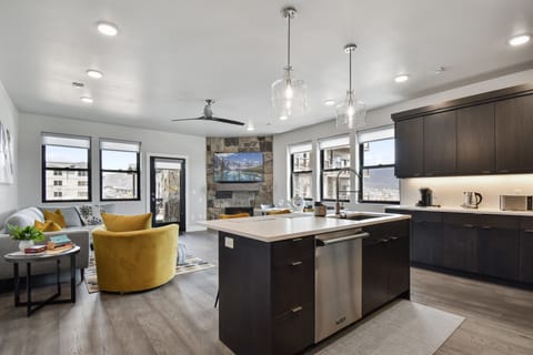 Bright, modern, and hip—this open space blends sleek kitchen finishes with vibrant living room accents. A bold mustard chair, stone fireplace, and large windows fill the area with light and personality, perfect for stylish everyday living.