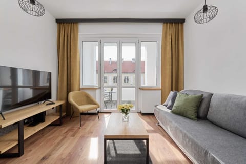 Bedroom features a gray sofa, a wooden coffee table, and a flat-screen TV, all illuminated by natural light from the balcony doors.