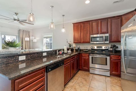 The fully equipped kitchen boasts warm wood cabinetry, stainless steel appliances, and ample granite countertop space for meal prep.