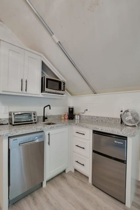 Well-equipped glamping tent with a modern kitchenette, including a dishwasher, fridge, and coffee maker, perfect for enjoying the comforts of home in a nature-filled setting.