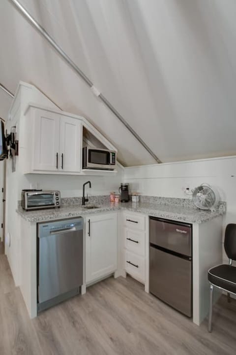 Well-equipped glamping tent with a modern kitchenette, including a dishwasher, fridge, and coffee maker, perfect for enjoying the comforts of home in a nature-filled setting.