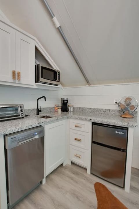 Glamping tent with a fully stocked kitchenette featuring a dishwasher, mini-fridge, microwave, and coffee maker, providing all the essentials for a hassle-free stay.