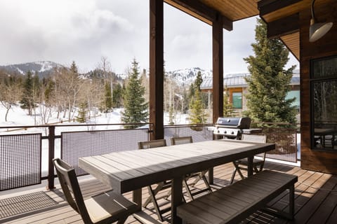 - Outdoor dining deck with grill and mountain views  
- Spacious wooden table perfect for family gatherings  
- Scenic backdrop of snow covered trees and peaks