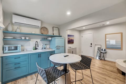 Bright studio w/ blue kitchenette, round dining table & cozy bed area in an open, airy layout