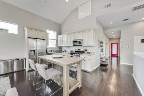 Open concept living room, dining room, and kitchen, hallway leads down to bedrooms, red door opens to the back deck.