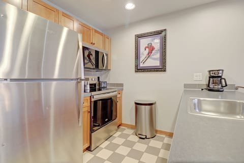 Your fully equipped kitchen awaits with gleaming stainless steel appliances and warm wood cabinets. The checkerboard floor adds charm while you brew morning coffee and prepare meals in this inviting space.