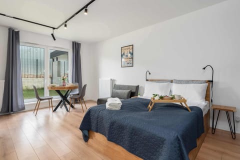 A cozy bedroom with a double bed, soft bedding, and minimalist decor, complemented by a nearby desk and a large window letting in natural light.
