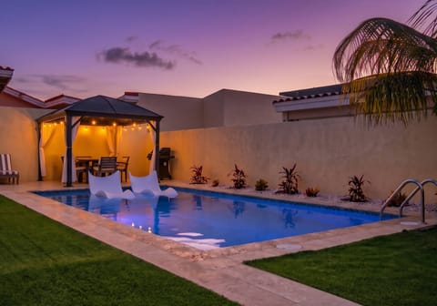 Evening ambiance by the private pool, featuring underwater lighting and a warm string-lit dining gazebo.