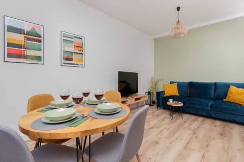 A bright and modern dining and living area with a round table, colorful chairs, and a blue sofa with yellow cushions.