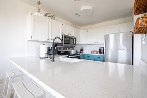 Kitchen bar with stainless steel appliances, fully stocked for cooking at home. Open layout flows to the dining area and deck, making meal prep easy while staying part of the conversation and views.