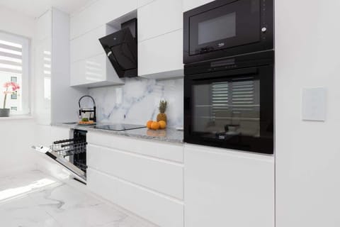 A modern kitchen with sleek white cabinetry, black appliances, and marble-style backsplash for a luxurious look.
